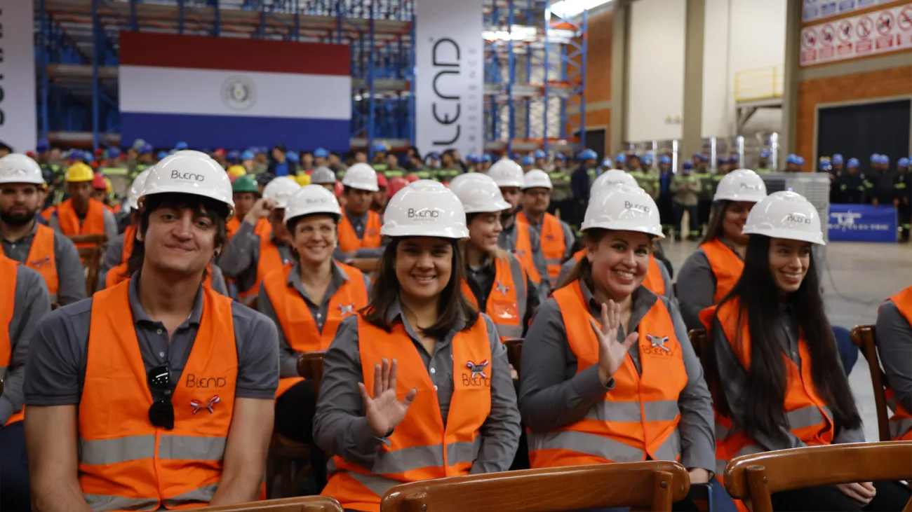 Trabajadores con casco y chaleco de seguridad en una fábrica en Paraguay, con la bandera paraguaya de fondo