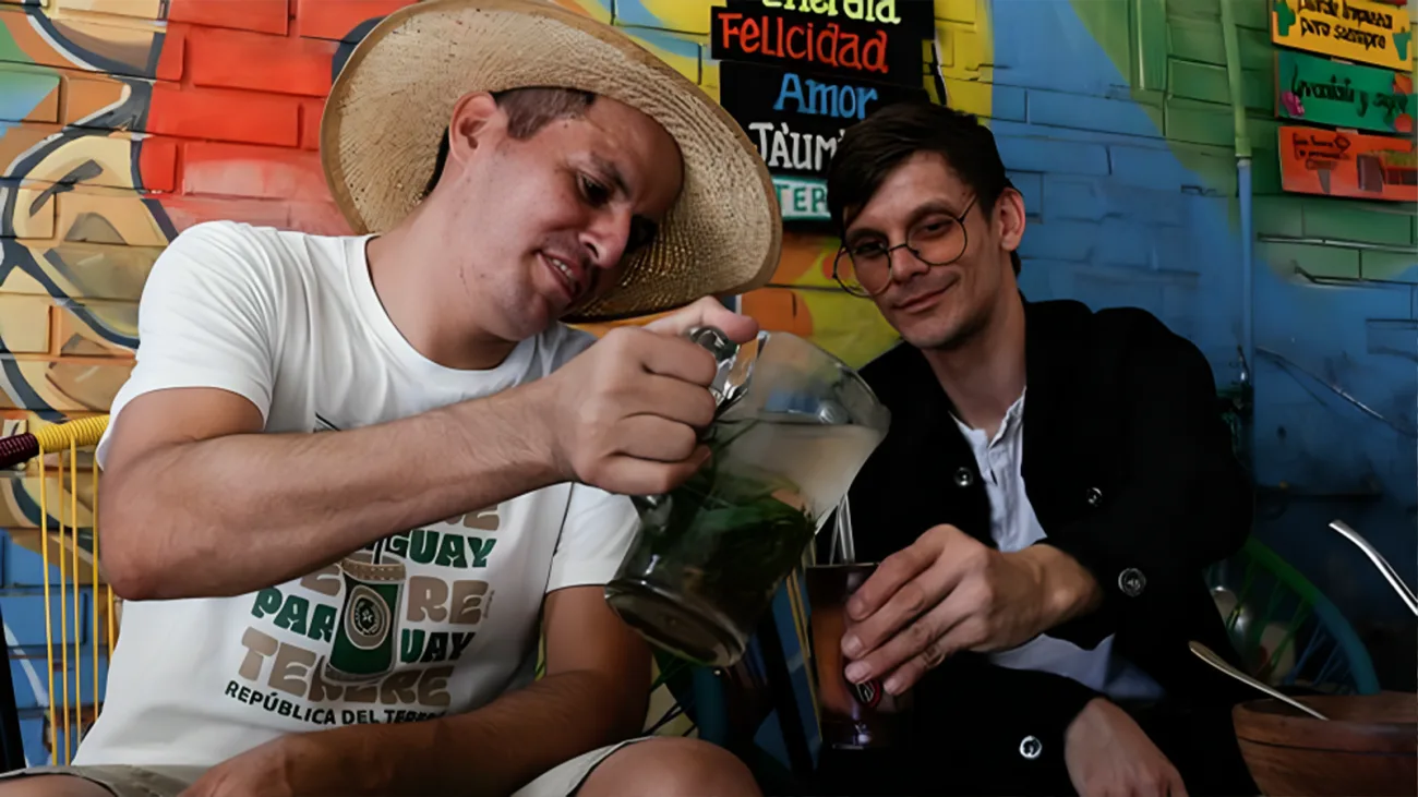 Two men drinking tereré, the traditional Paraguayan iced yerba mate, in front of a colorful street mural
