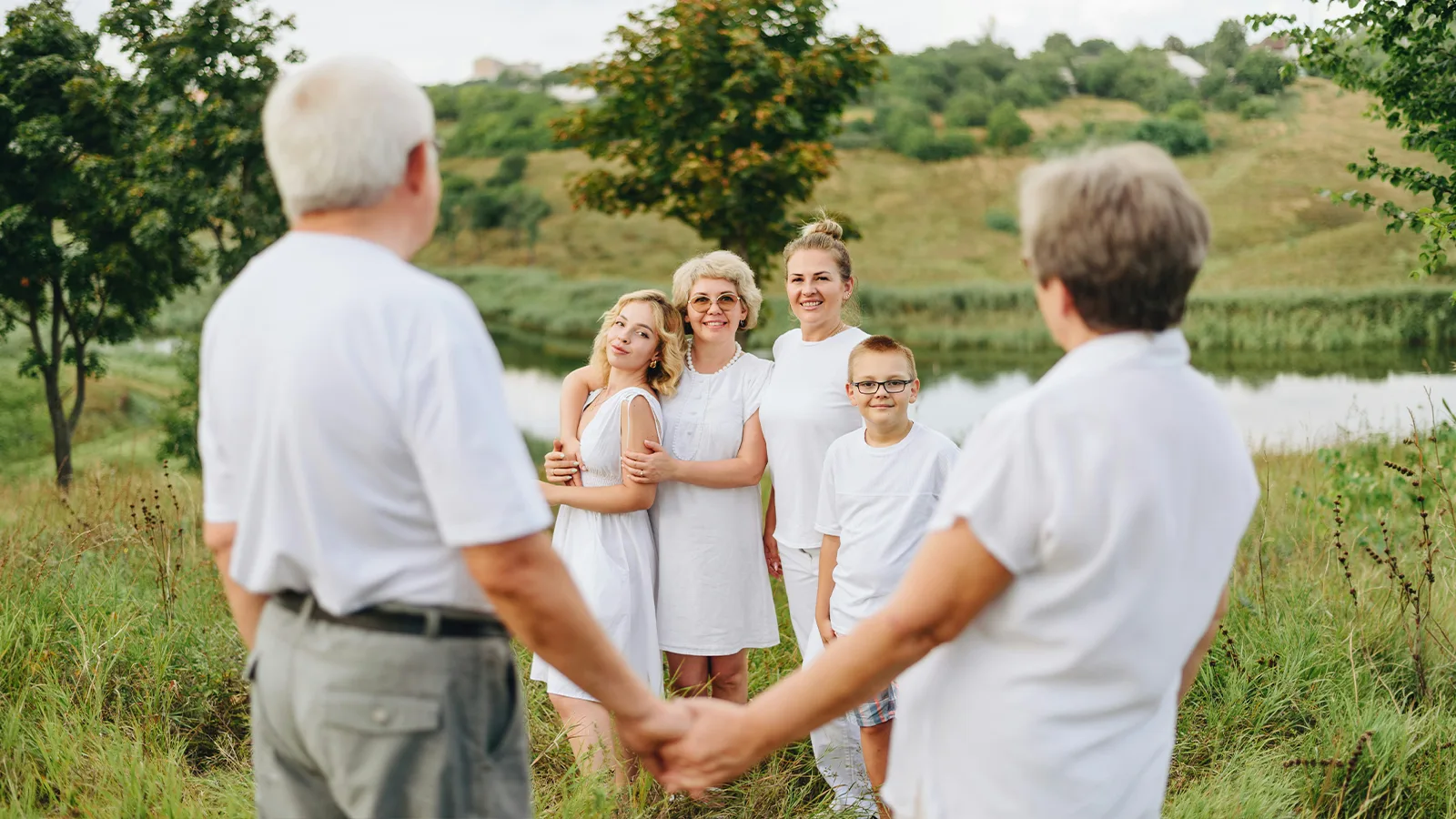 Família de três gerações de mãos dadas formando um círculo em um campo aberto