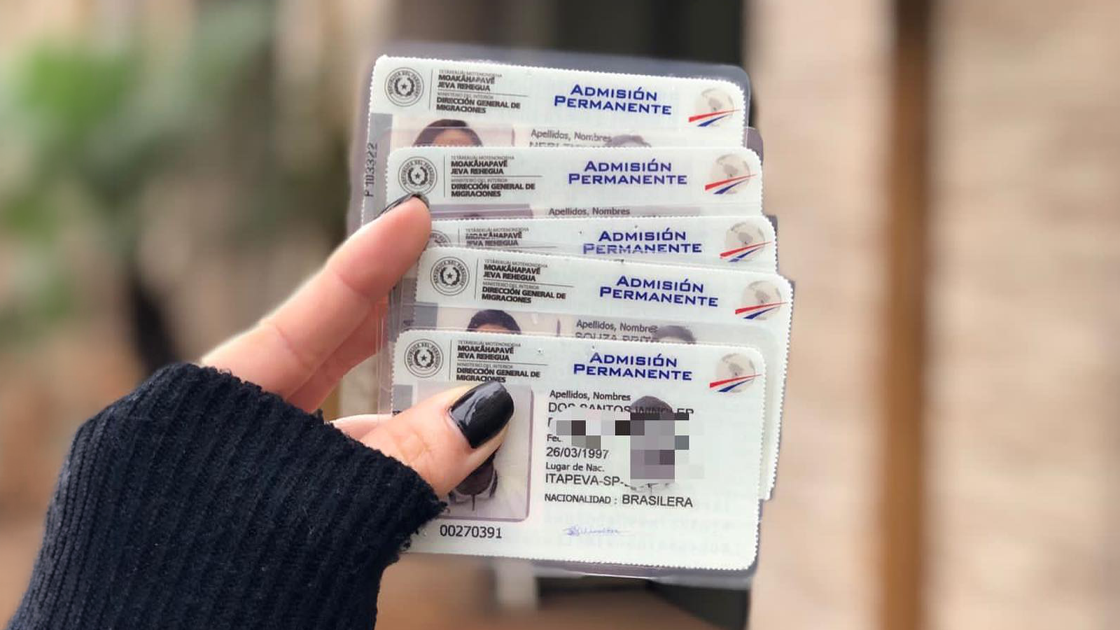 Hand holding several Permanent Admission residency cards issued by Paraguay's immigration authority
